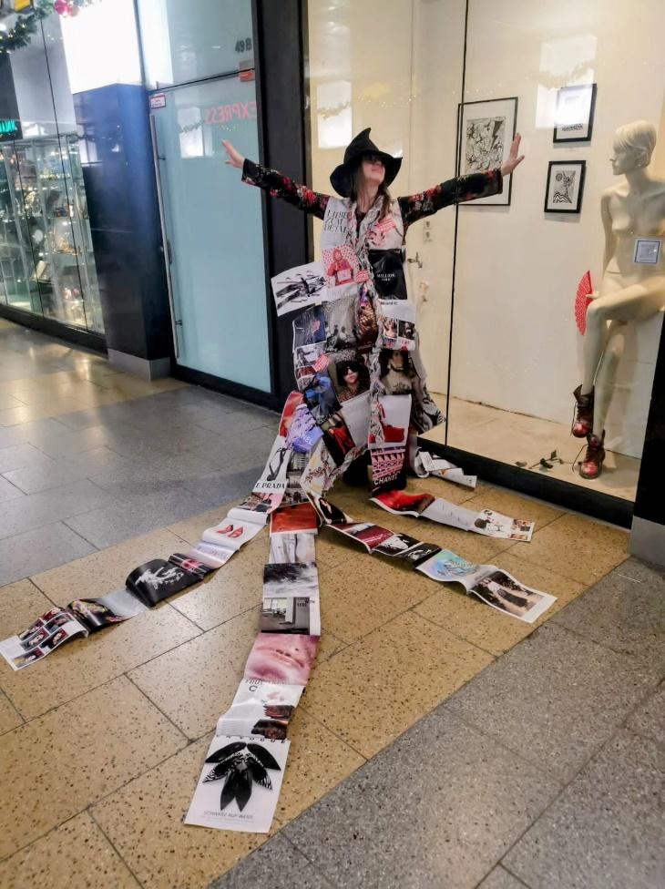 A collage fashion performance with a paper costume and a long collage train in an exhibition space.
