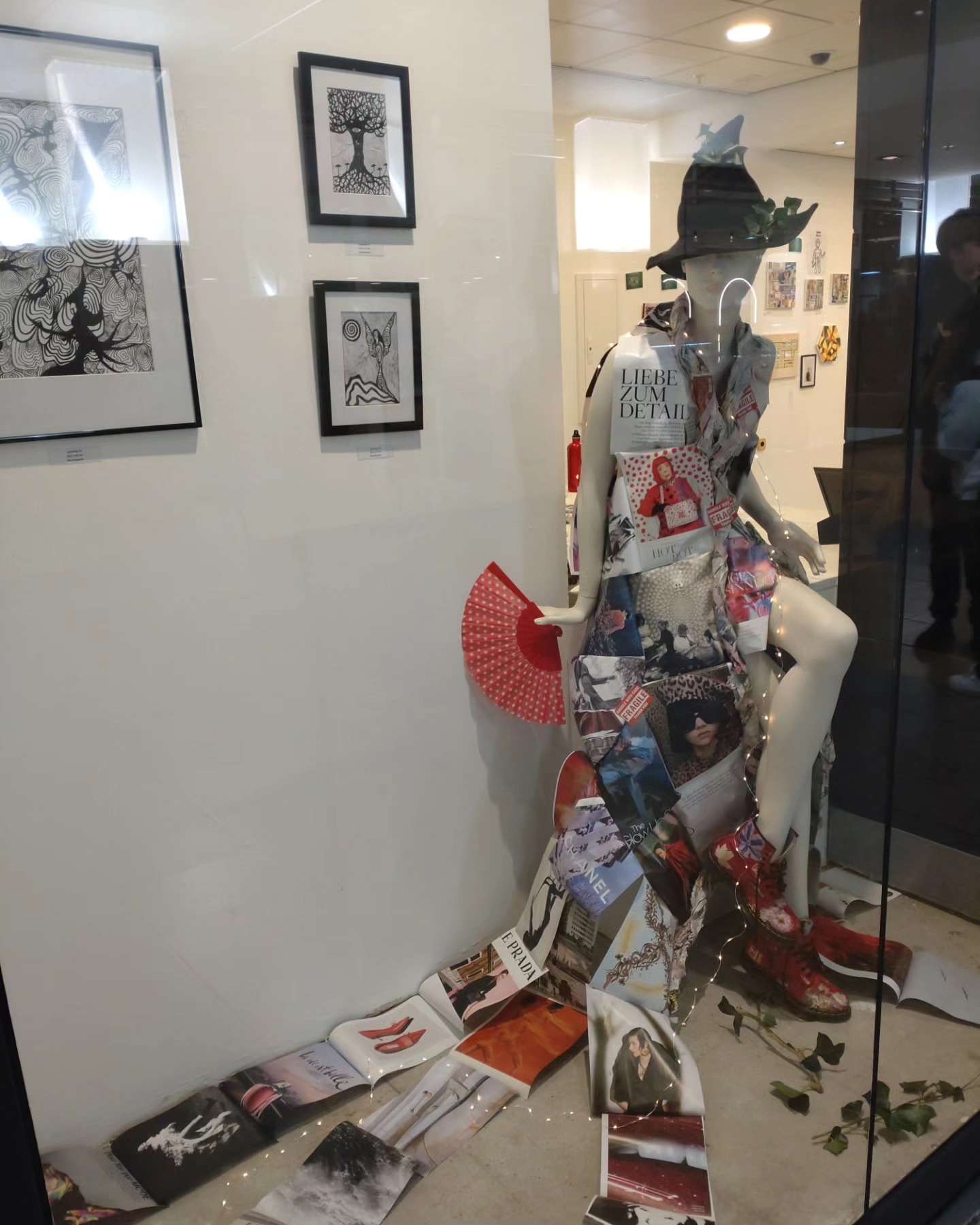 A collage-fashion witch mannequin surrounded by framed artworks in the window of the AUSGEUFERT exhibition in Hannover, Germany.