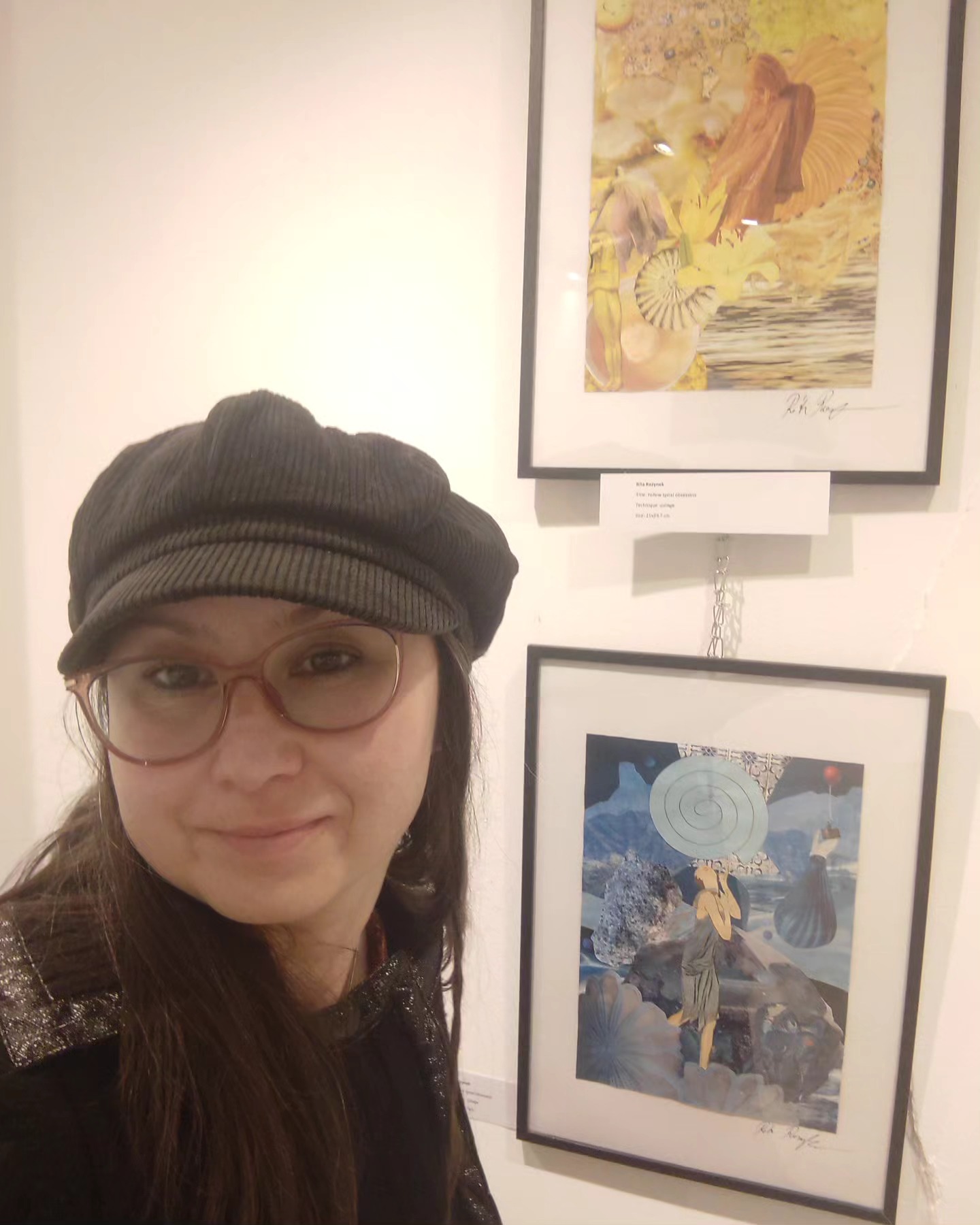 Rita Rozynek taking a selfie beside two framed collages at the 3F Art Gallery in Paris.